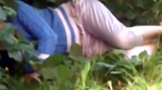 Drunk woman caught trying to pee beyond some bushes falls in the grass.